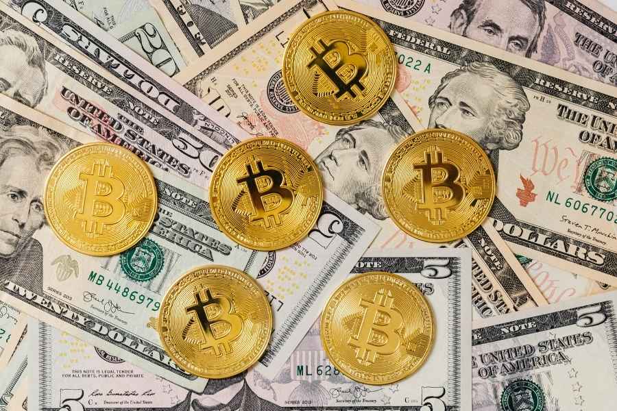 Plusieurs pièces de Bitcoin dorées sont disposées sur un fond de billets de banque, illustrant la rencontre entre monnaie traditionnelle et finance décentralisée.