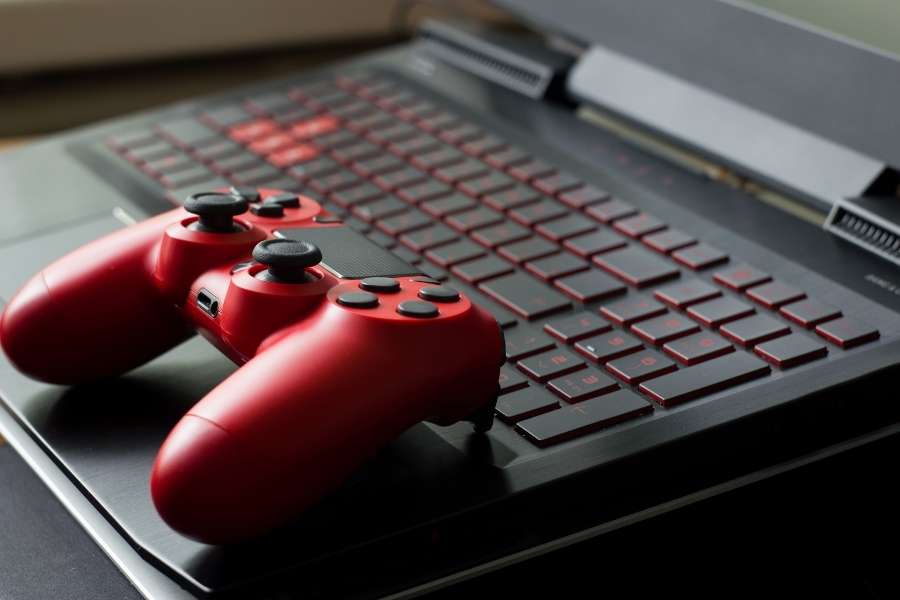 Une manette rouge sans fil posée sur le clavier rétroéclairé d'un ordinateur portable de jeu.